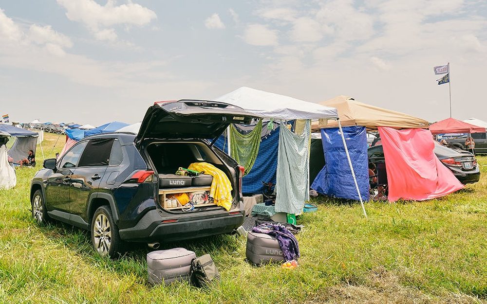 A tent and shade set up alongside a parked car on a vehicle camping plot